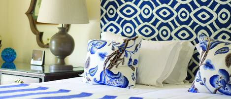 A neatly made bed with blue and white striped bedding, a patterned pillow, a bedside lamp, and a decorative mirror on a nightstand.