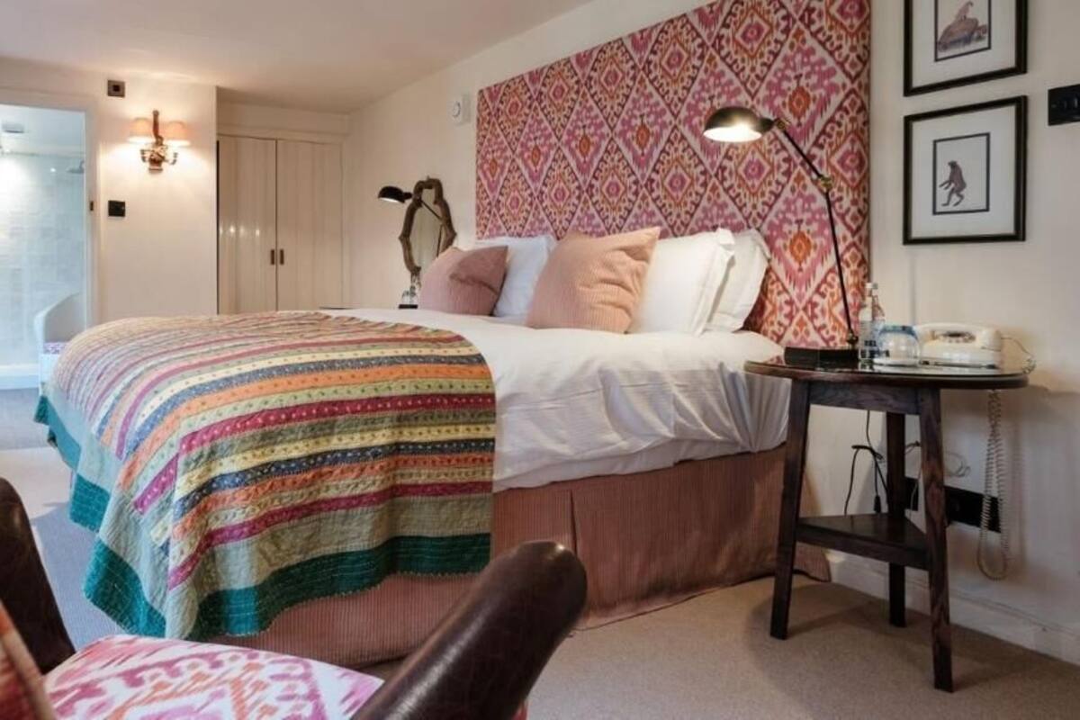 Quarto com cama, mesa de cabeceira, abajur e cabeceira estampada.