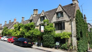 A row of traditional stone buildings with steeply pitched roofs, parked cars, and a clear blue sky. - Bay Tree Hotel (Burford)