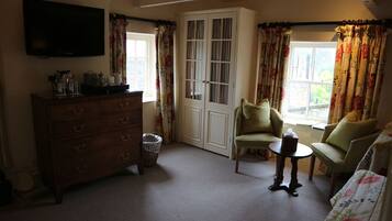 A cozy room with a wooden dresser, a television, a window with floral curtains, and a green armchair.