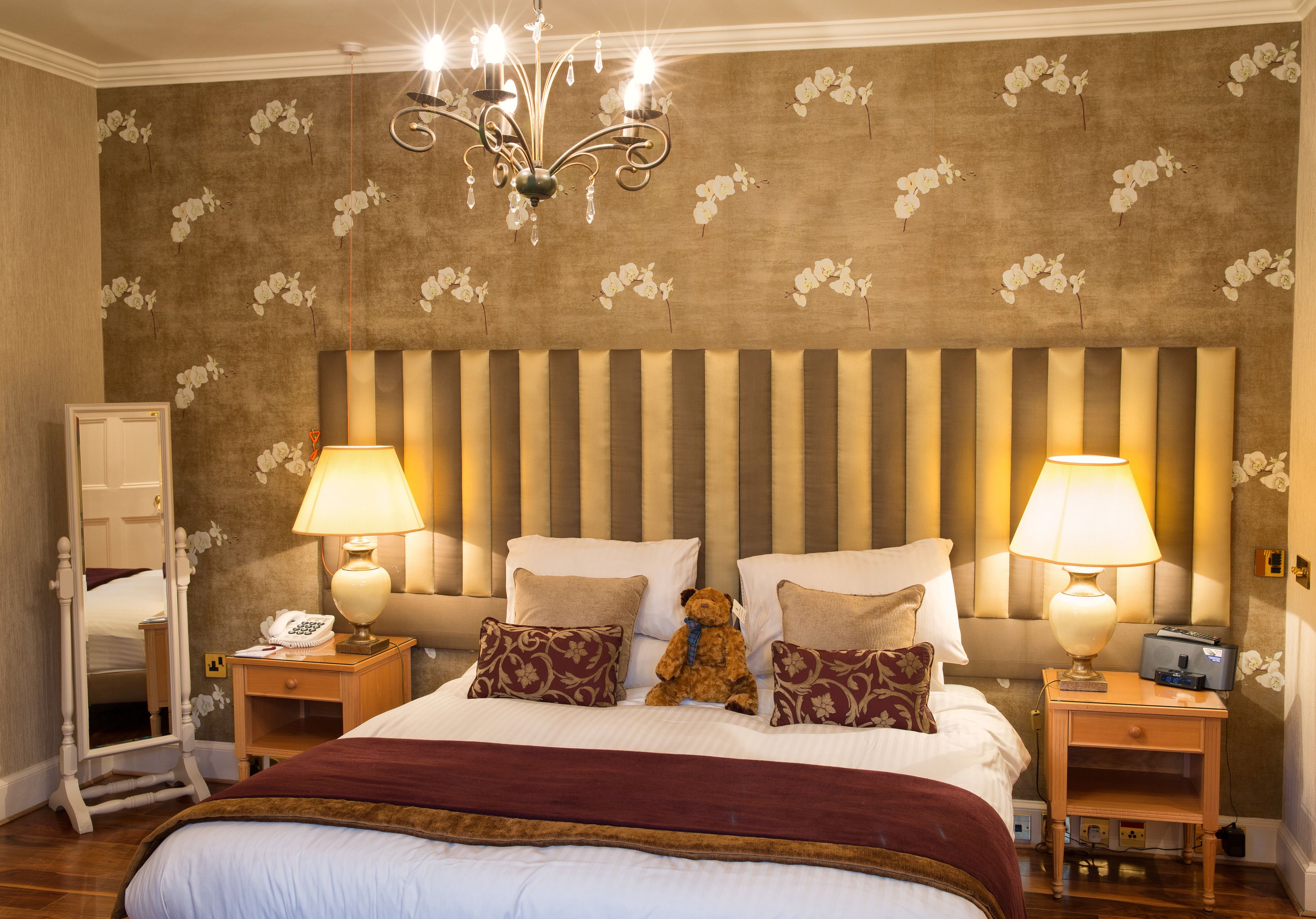 A hotel room with a large bed, two bedside tables, a mirror, and a chandelier.