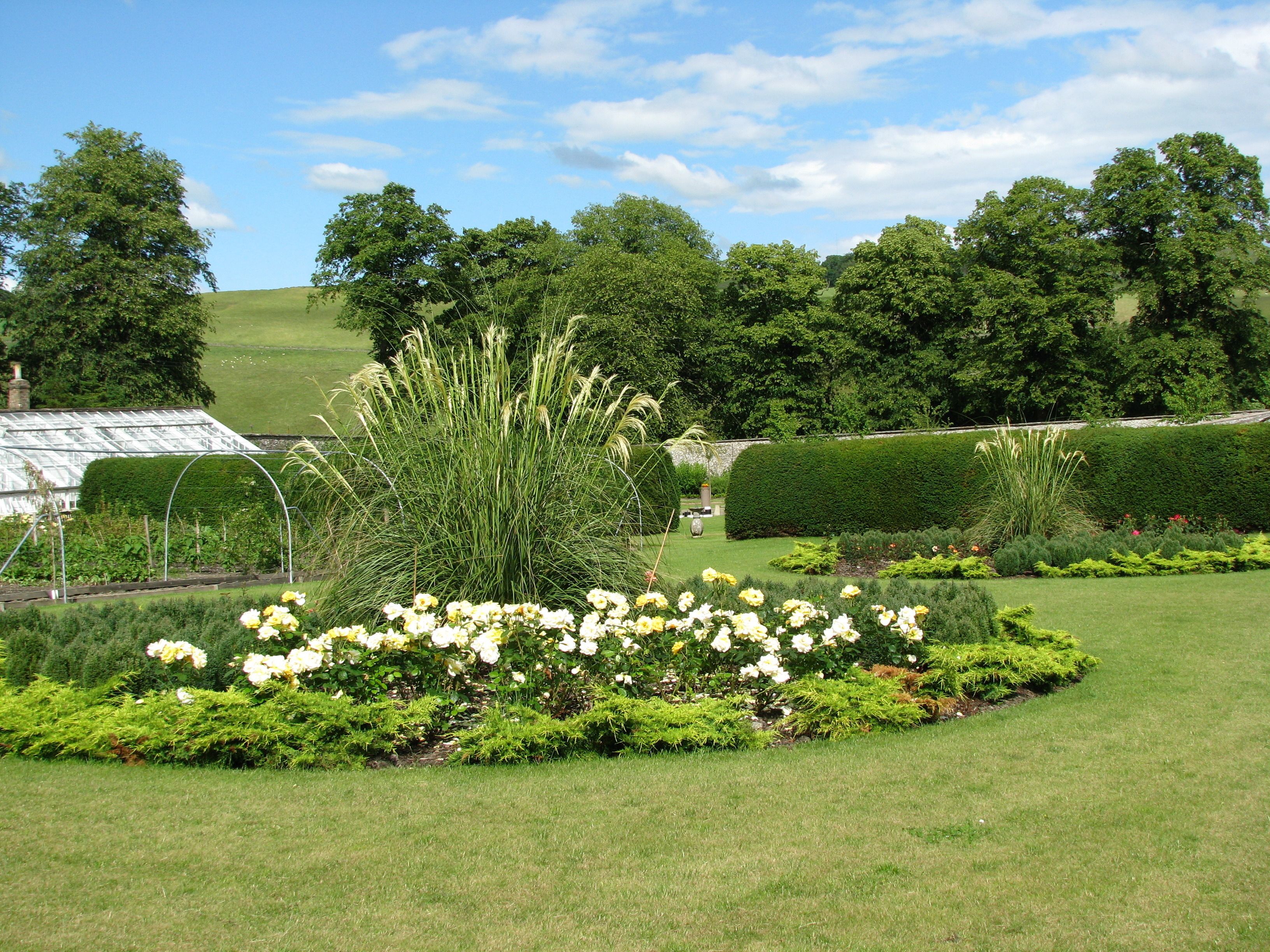A well-maintained garden with a variety of plants and flowers, a greenhouse, and neatly trimmed hedges.