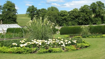 A well-maintained garden with a variety of plants and flowers, a greenhouse, and neatly trimmed hedges.