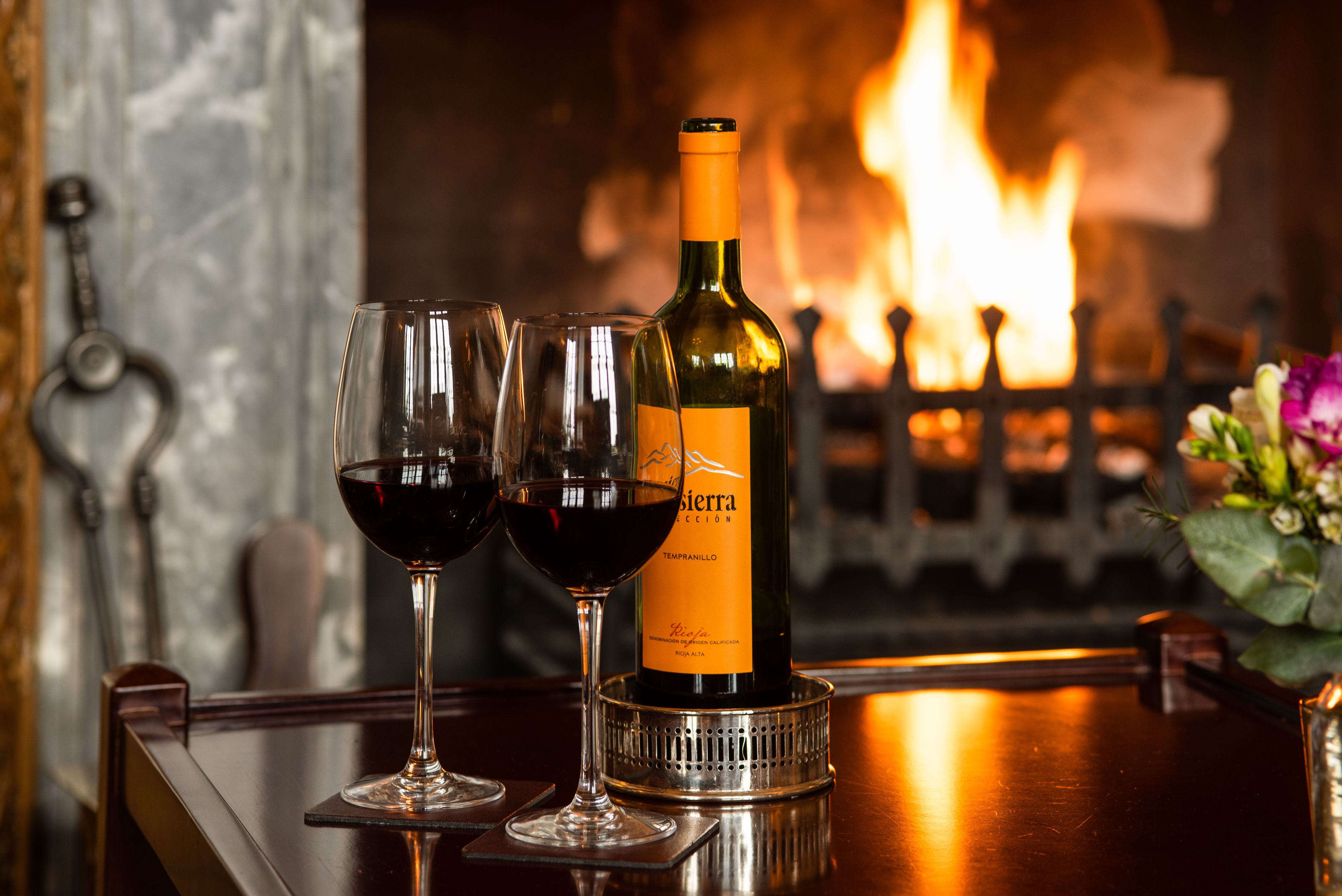 Una botella de vino y dos copas sobre una barra con una chimenea al fondo.