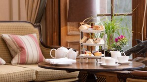 A dining table with a tiered tray of sandwiches, a teapot, cups, saucers, and a vase with flowers. - Cringletie House Hotel (Peebles)