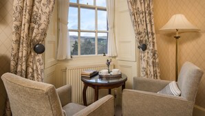 A room with two armchairs, a small round table with a book and a vase, and a view through a window with curtains. - Cringletie House Hotel (Peebles)