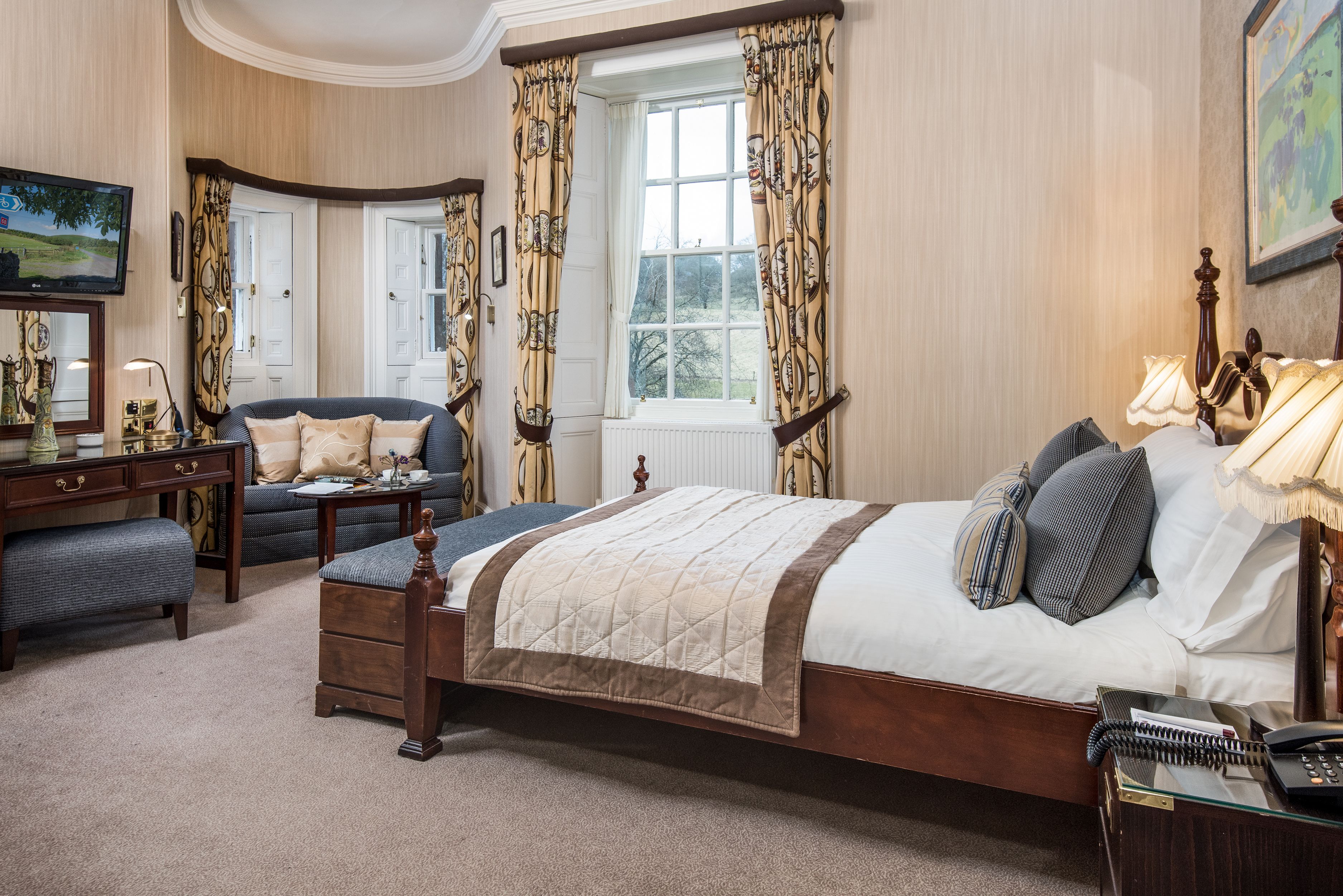 Een slaapkamer met een groot bed, een bureau, een stoel en een raam met gordijnen.