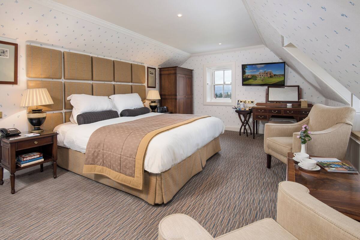 Habitación de hotel con una cama grande, un escritorio, una silla, un televisor y una ventana.