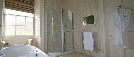 A bathroom with a large bathtub, a glass-enclosed shower, and a white robe hanging on the door.