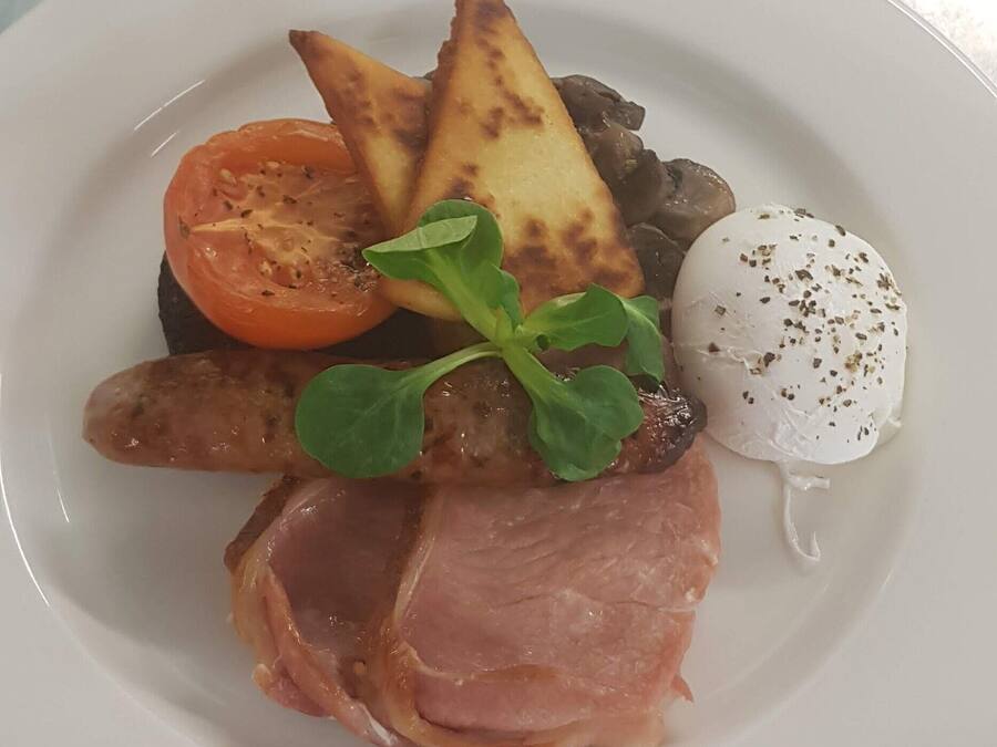 A plate with a slice of ham, a poached egg, grilled mushrooms, roasted potatoes, and a slice of tomato.