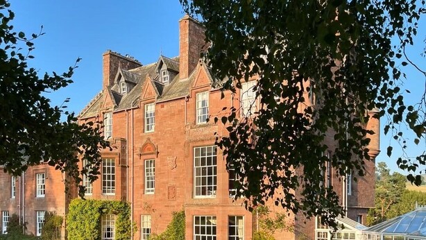 A large brick building with a well-maintained lawn, a conservatory, and a wooden fence. - Cringletie House Hotel (Peebles)