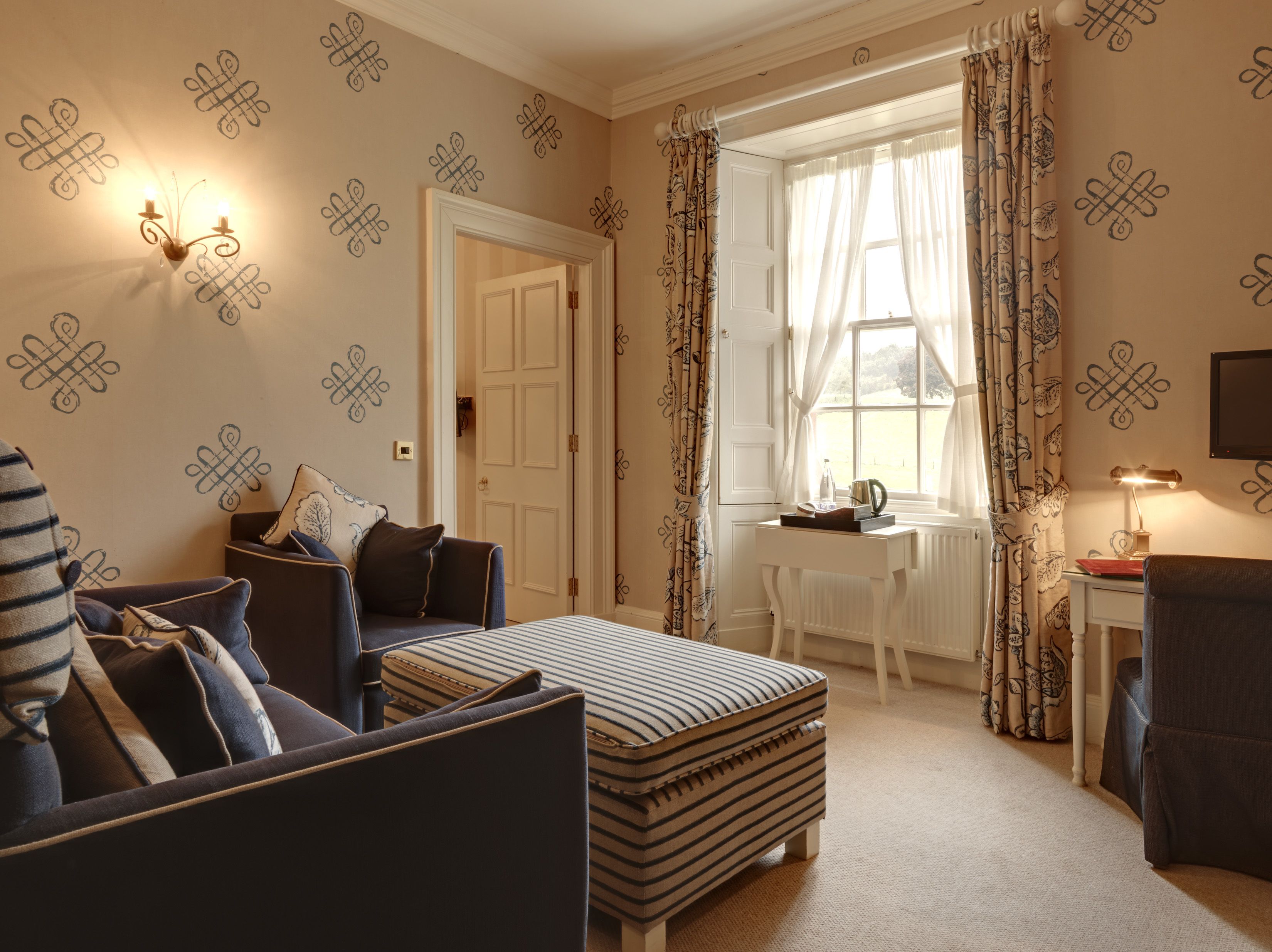A room with a bed, a desk, and a chair. There is a door leading to another room.