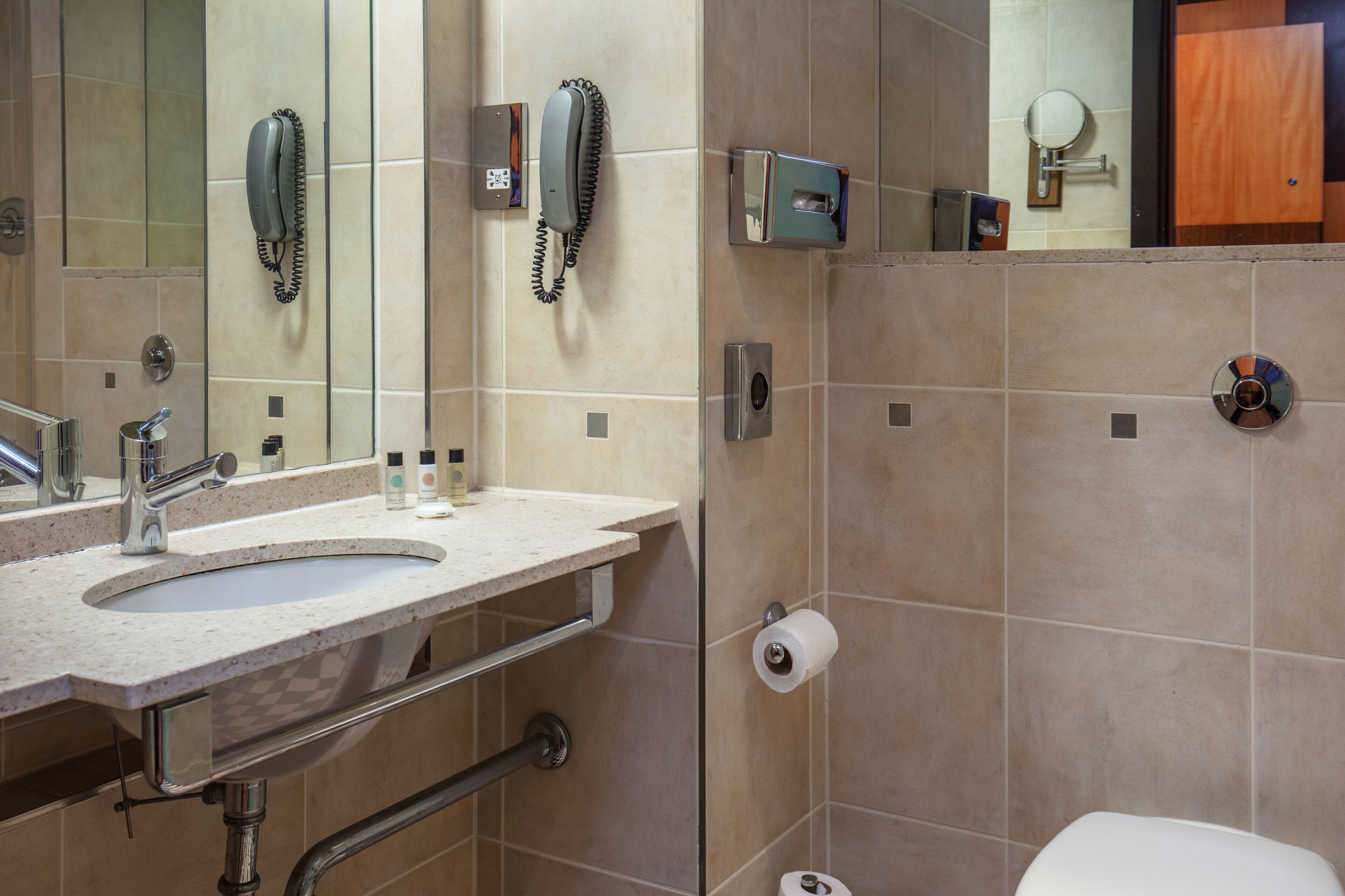 Un baño con lavamanos, espejo, inodoro y teléfono.