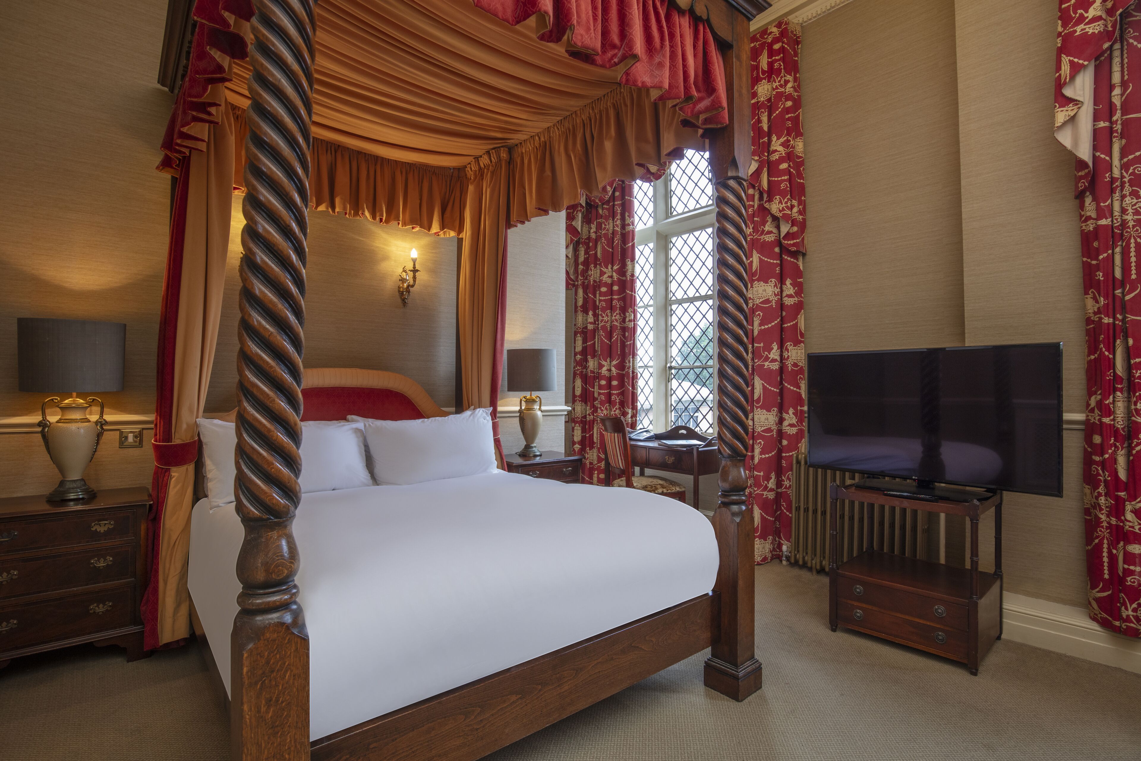 A four-poster bed with a canopy, a television on a stand, and a desk with a lamp.