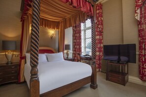 A four-poster bed with a canopy, a television on a stand, and a desk with a lamp.