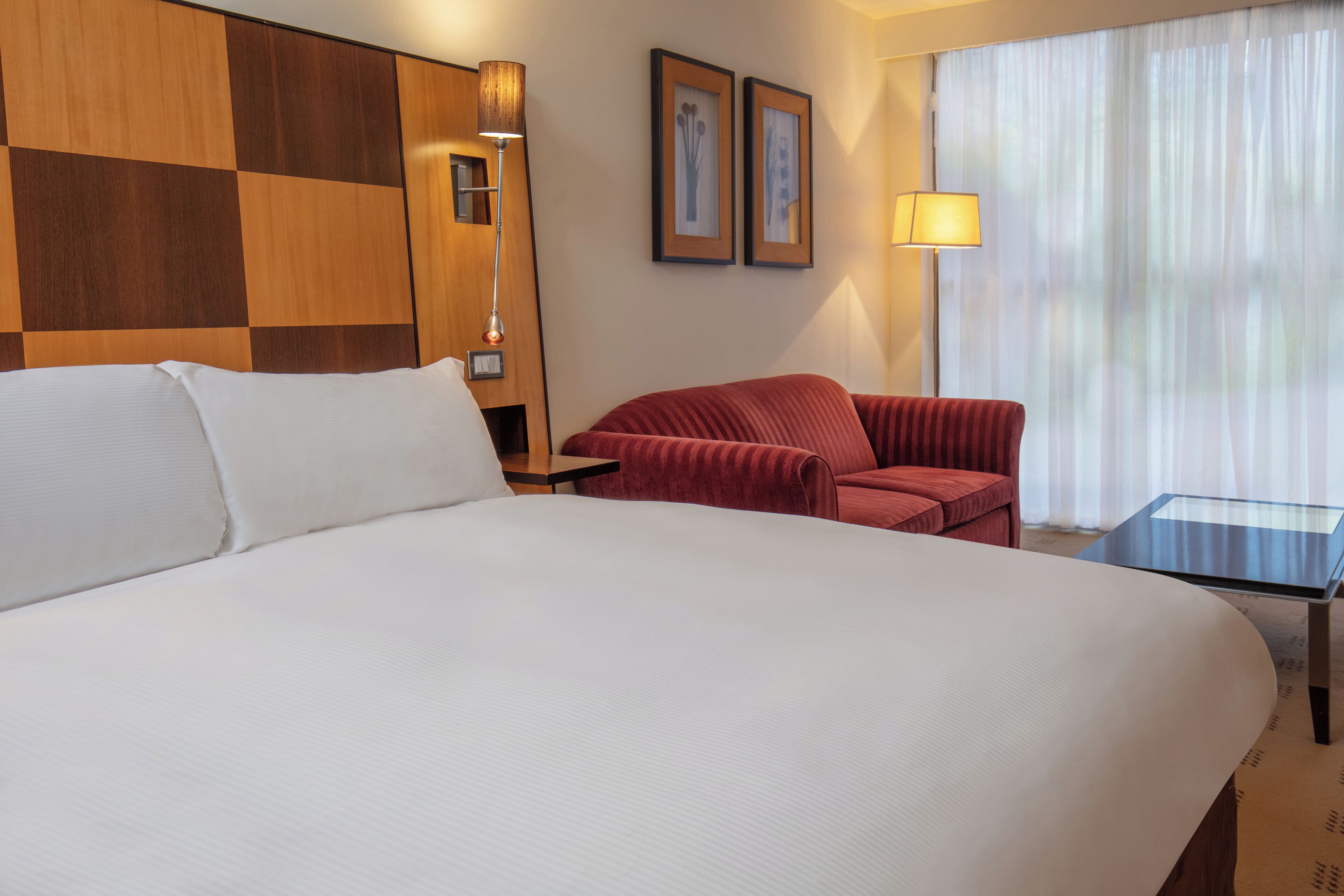 Een hotelkamer met een groot bed, een rode fauteuil, een klein tafeltje en een lamp.
