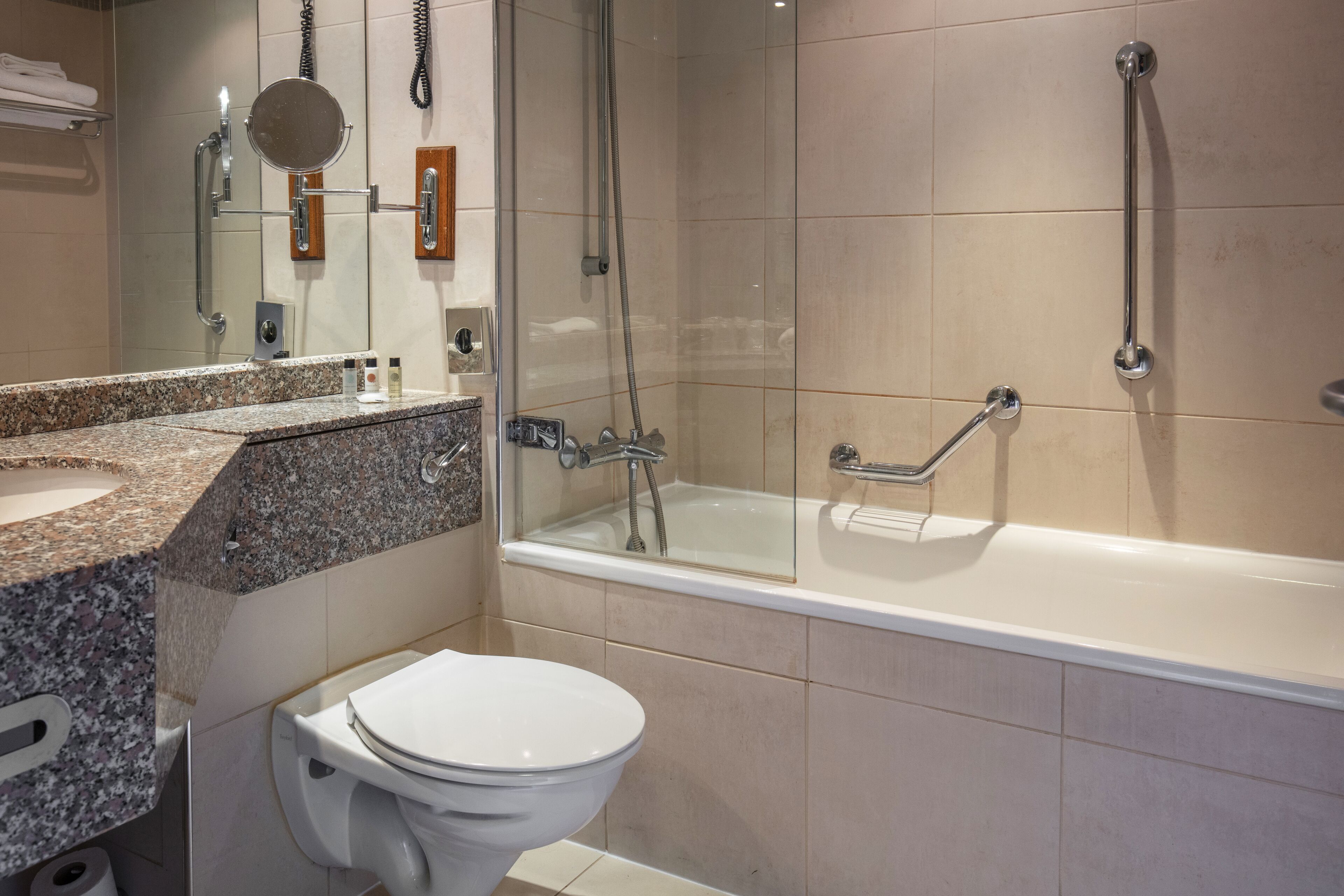 Une salle de bain moderne avec un comptoir en granit, des toilettes blanches, une douche à parois de verre et une baignoire.