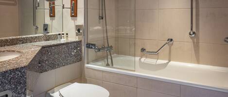 Une salle de bain moderne avec un comptoir en granit, des toilettes blanches, une douche à parois de verre et une baignoire.
