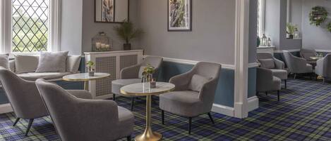 A room with a plaid carpet, grey upholstered chairs, a round table, and a window with a view.
