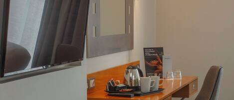 Una habitación de hotel con un escritorio de madera, una silla, un reposapiés azul, un espejo y dos lámparas fijadas a la pared.