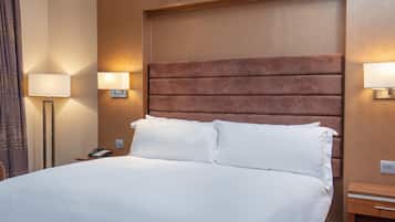 A hotel room with a large bed, two bedside lamps, a nightstand, and a wall-mounted light fixture.
