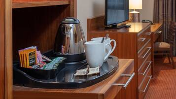 A hotel room with a wooden desk, a coffee maker, a white mug, and a tray with breakfast items.