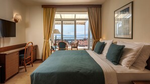 A hotel room with a bed, a desk, a chair, a TV, and a large window with curtains.