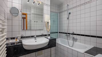 Un baño moderno con un lavamanos blanco, encimera negra y una bañera independiente.