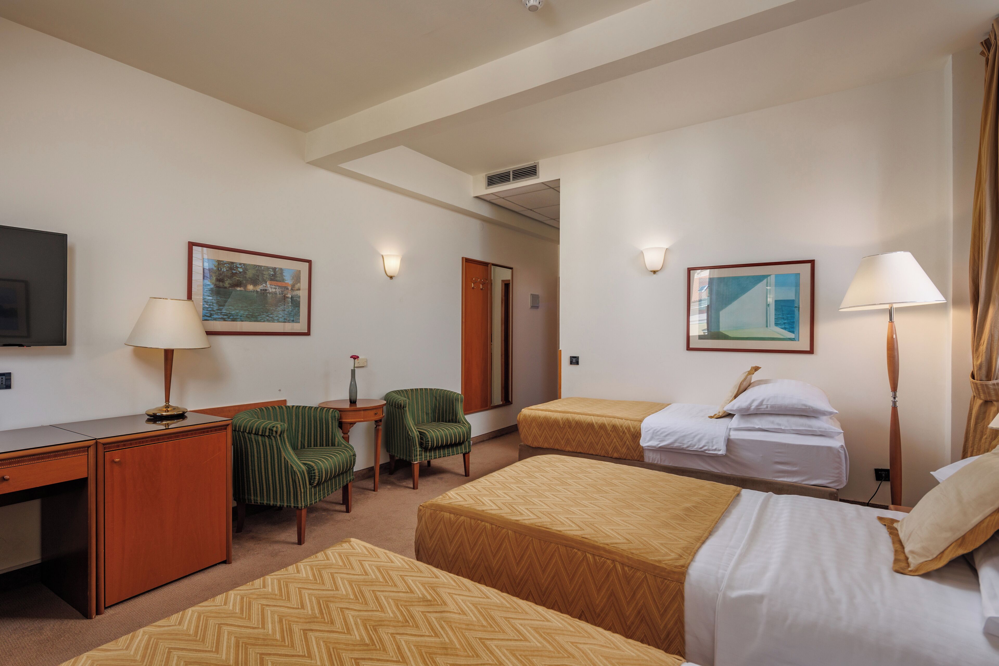 Ein Hotelzimmer mit zwei Betten, einem Schreibtisch, einem Sessel, einem Fernseher und Bildern an den Wänden.
