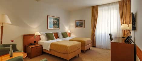 Quarto de hotel com duas camas, uma escrivaninha, uma cadeira, uma televisão e um abajur.