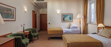 Habitación de hotel con dos camas, un escritorio, una silla, una lámpara y un cuadro en la pared.