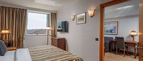 A hotel room with a bed, a desk, a chair, a dresser, and a large window.