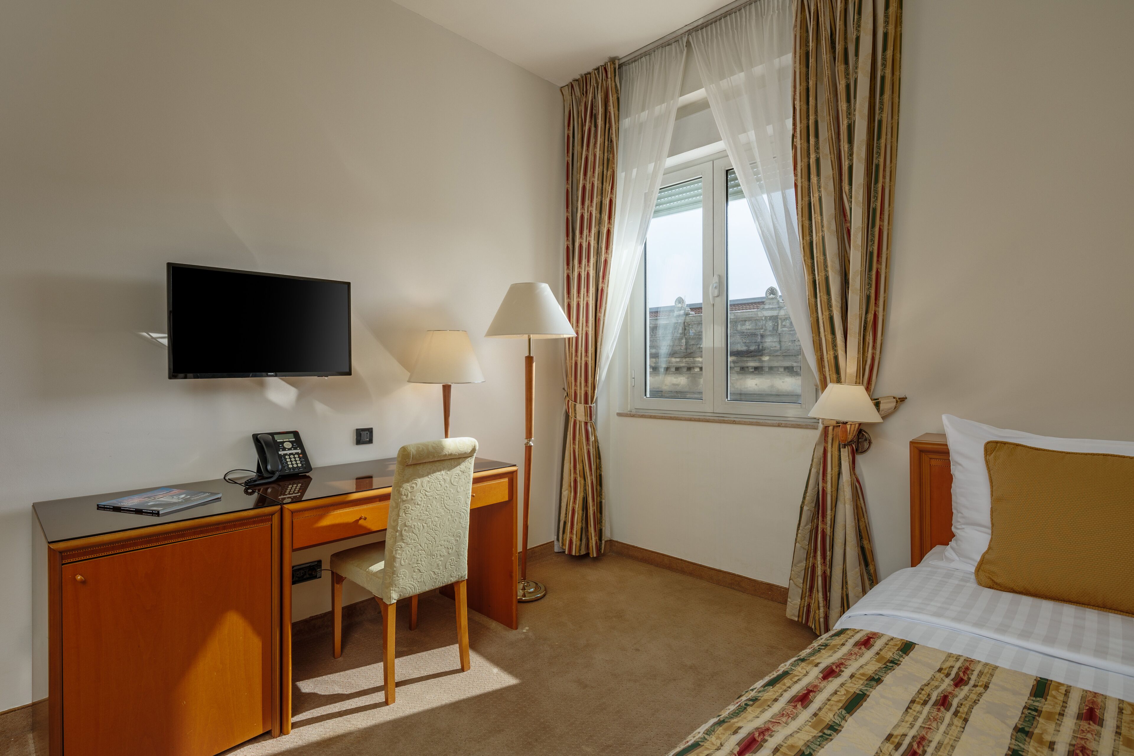 A hotel room with a bed, desk, chair, television, and curtains.