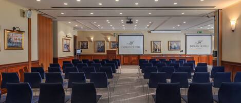 Uma sala de conferências com fileiras de cadeiras, um pódio e telas de apresentação.