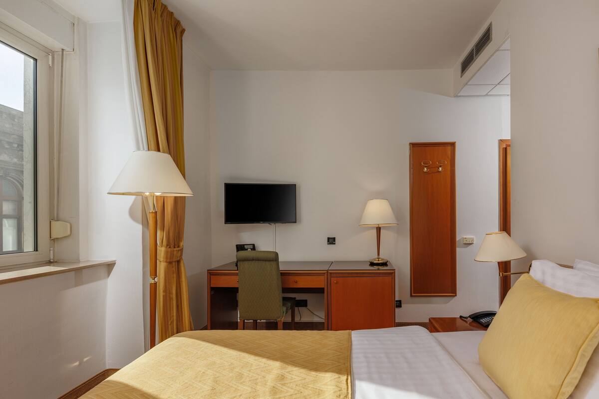 Una habitación de hotel con cama, escritorio, silla, televisión y armario.