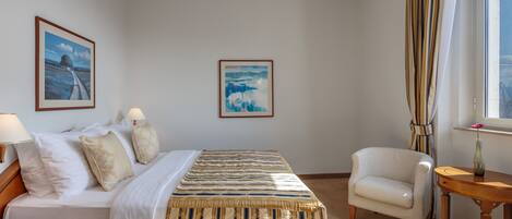 A hotel room with a bed, two chairs, a small table, and two framed pictures on the wall.