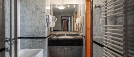 Un baño con piso de mármol, una bañera, un lavamanos con espejo y un perchero para toallas.