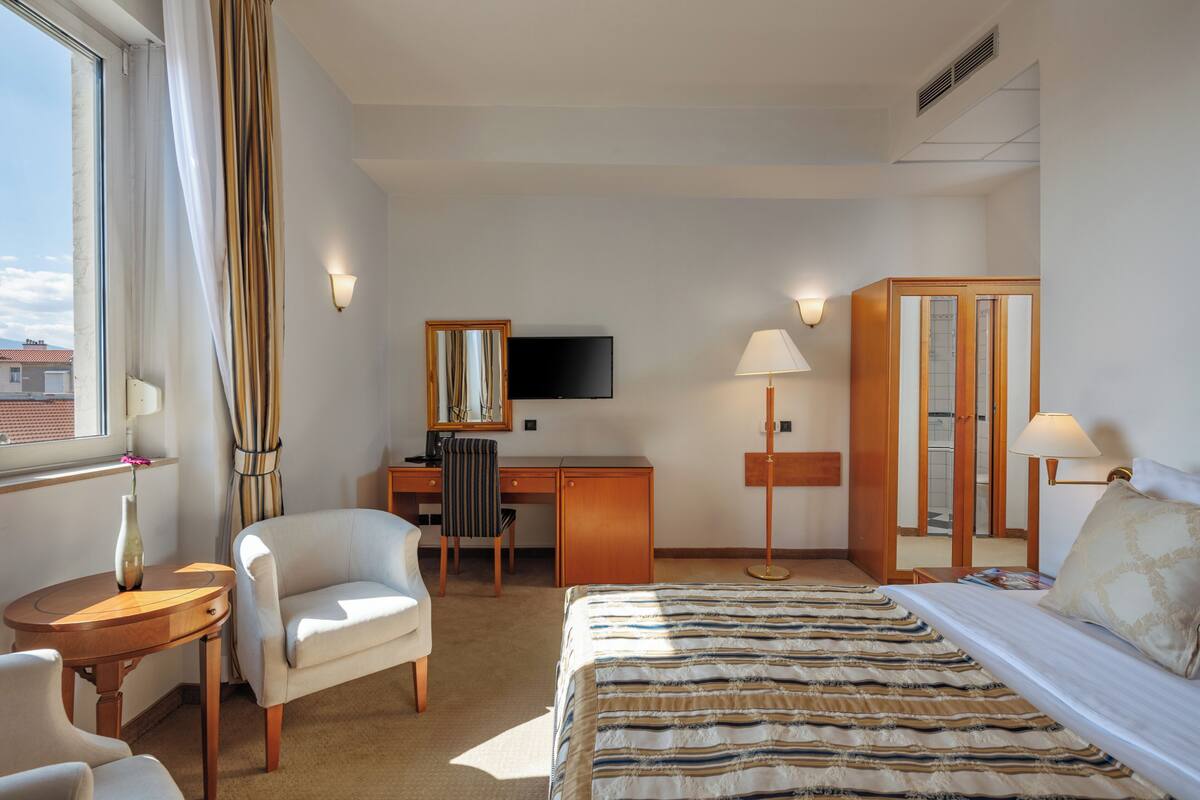 Una habitación de hotel con cama, escritorio, silla, televisor y armario.