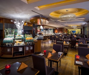A restaurant with a buffet, multiple dining tables, and a chandelier.