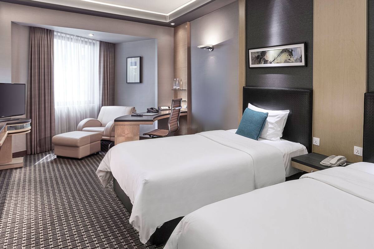 Une chambre d’hôtel avec deux lits, un bureau avec un ordinateur, une télévision et une salle de bain visible à travers une porte ouverte.