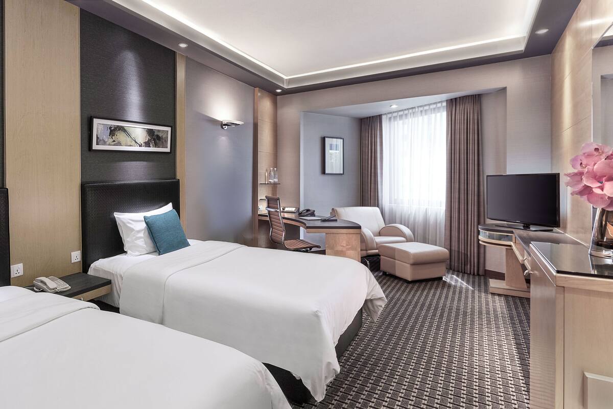Une chambre d’hôtel avec deux lits, un bureau, une chaise, une télévision et une salle de bain visible à travers une porte ouverte.