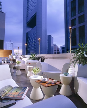 A rooftop lounge with modern seating, a tray with teaware, and a view of tall buildings.