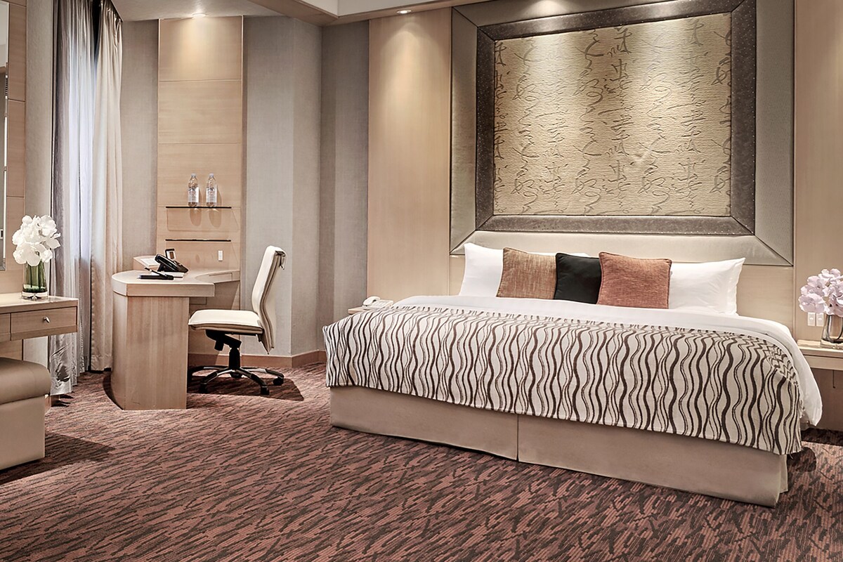 A modern hotel room with a large bed, a desk, and a chair.