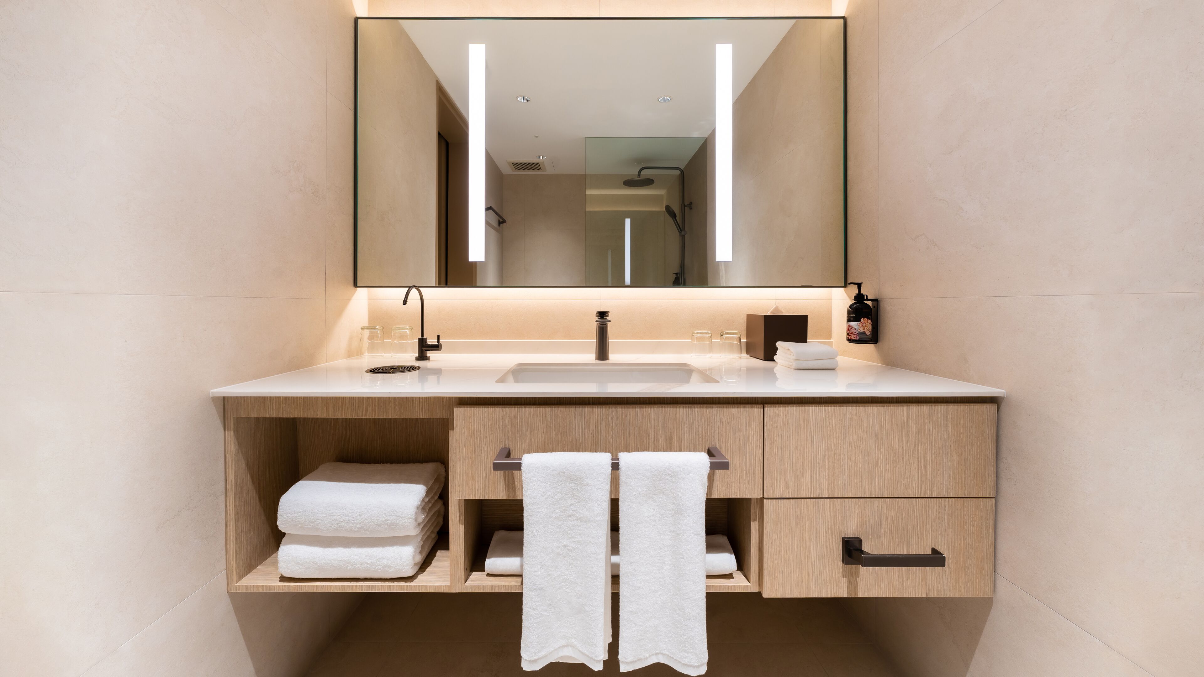 Un baño moderno con un espejo grande, un lavamanos, un perchero para toallas y un armario.
