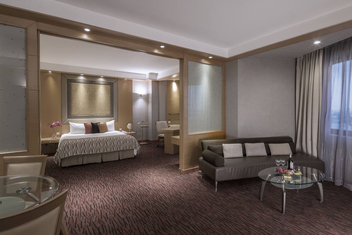 Une chambre d’hôtel avec un lit, un canapé, une table basse en verre et un bureau.