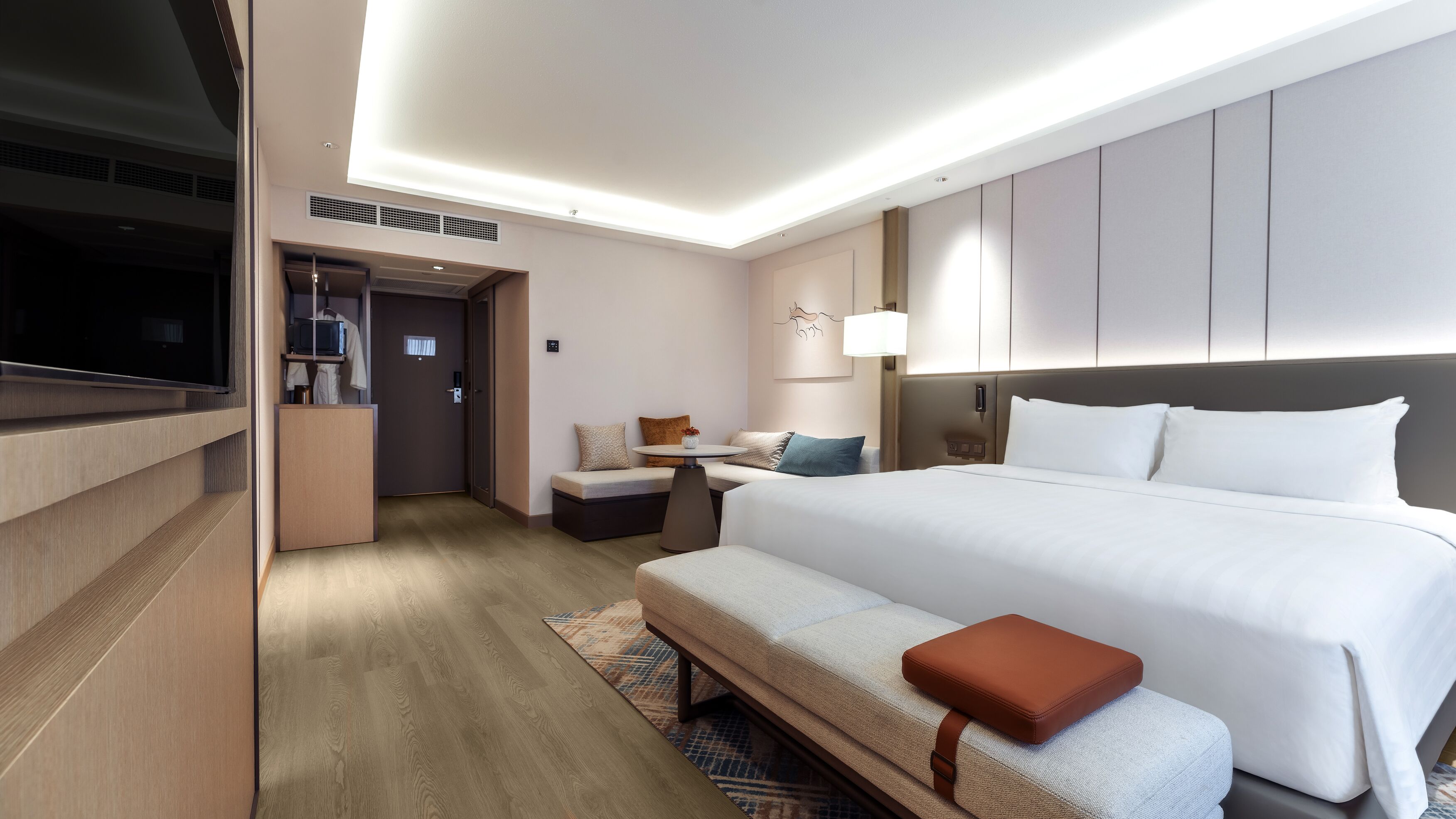 A modern hotel room with a large bed, a desk, a television, and a seating area.
