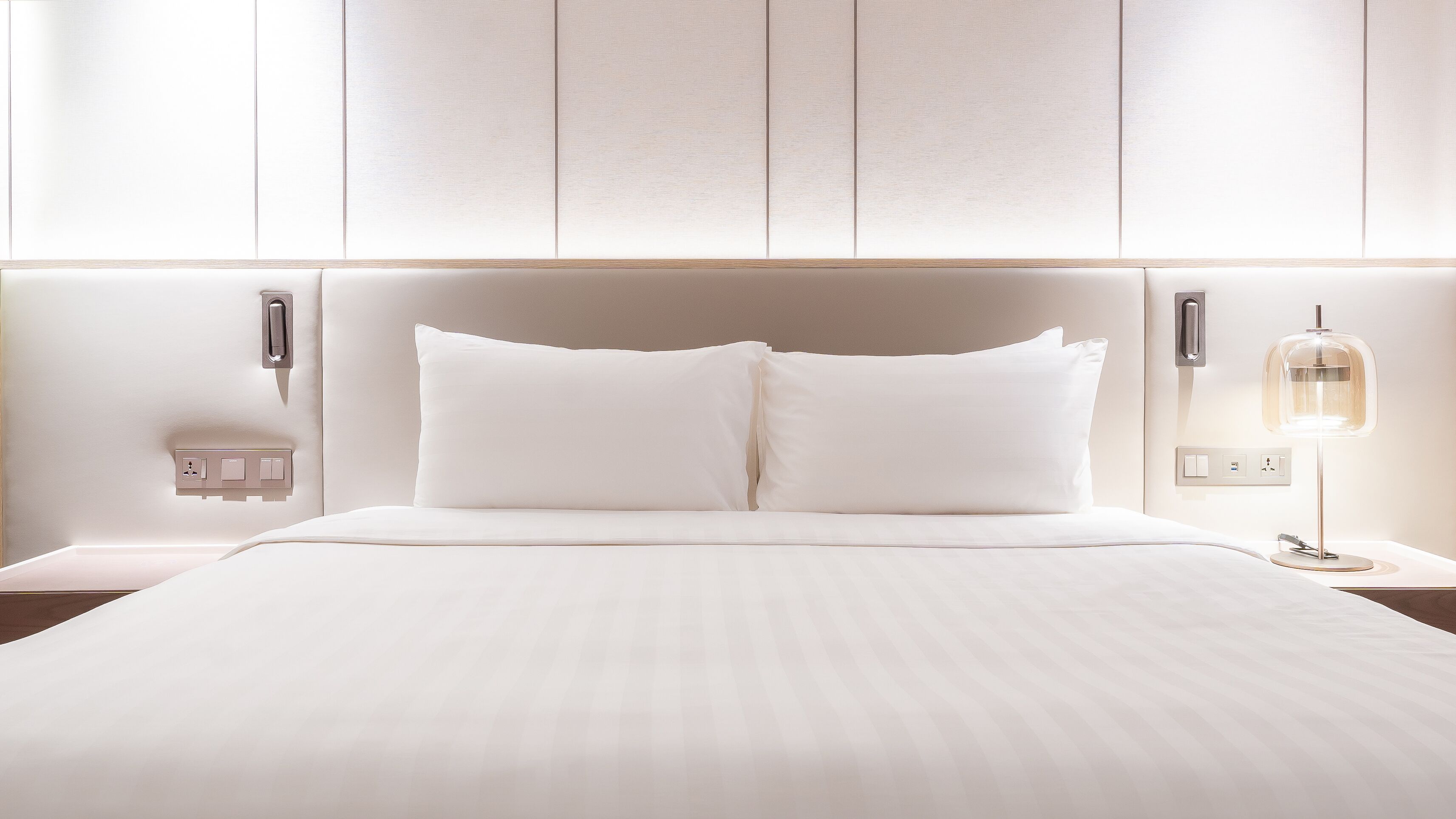 A neatly made bed with a headboard, bedside tables, and a lamp.
