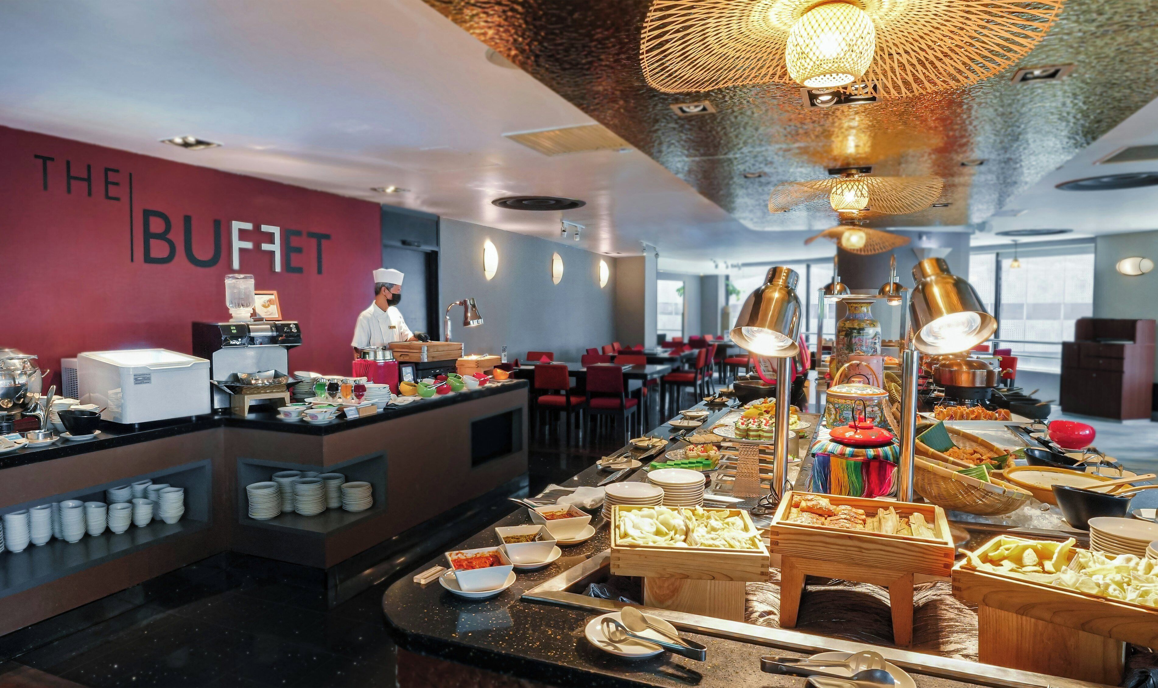 Buffet preparat amb un cuiner, diferents espais de menjar i una paret vermella amb la indicació 'THE BUFFET'.