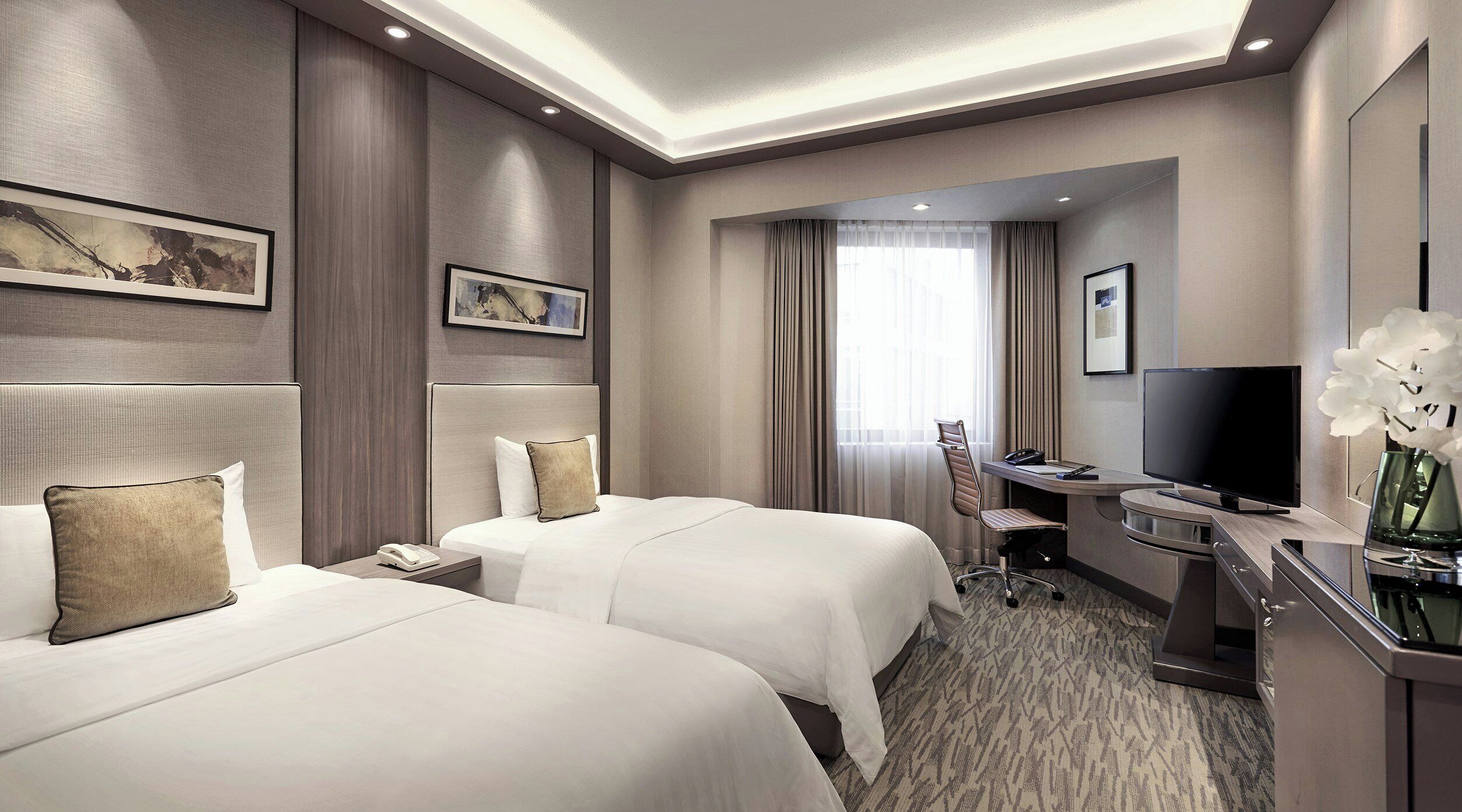 A hotel room with two beds, a desk with a chair, a television, and a bathroom.