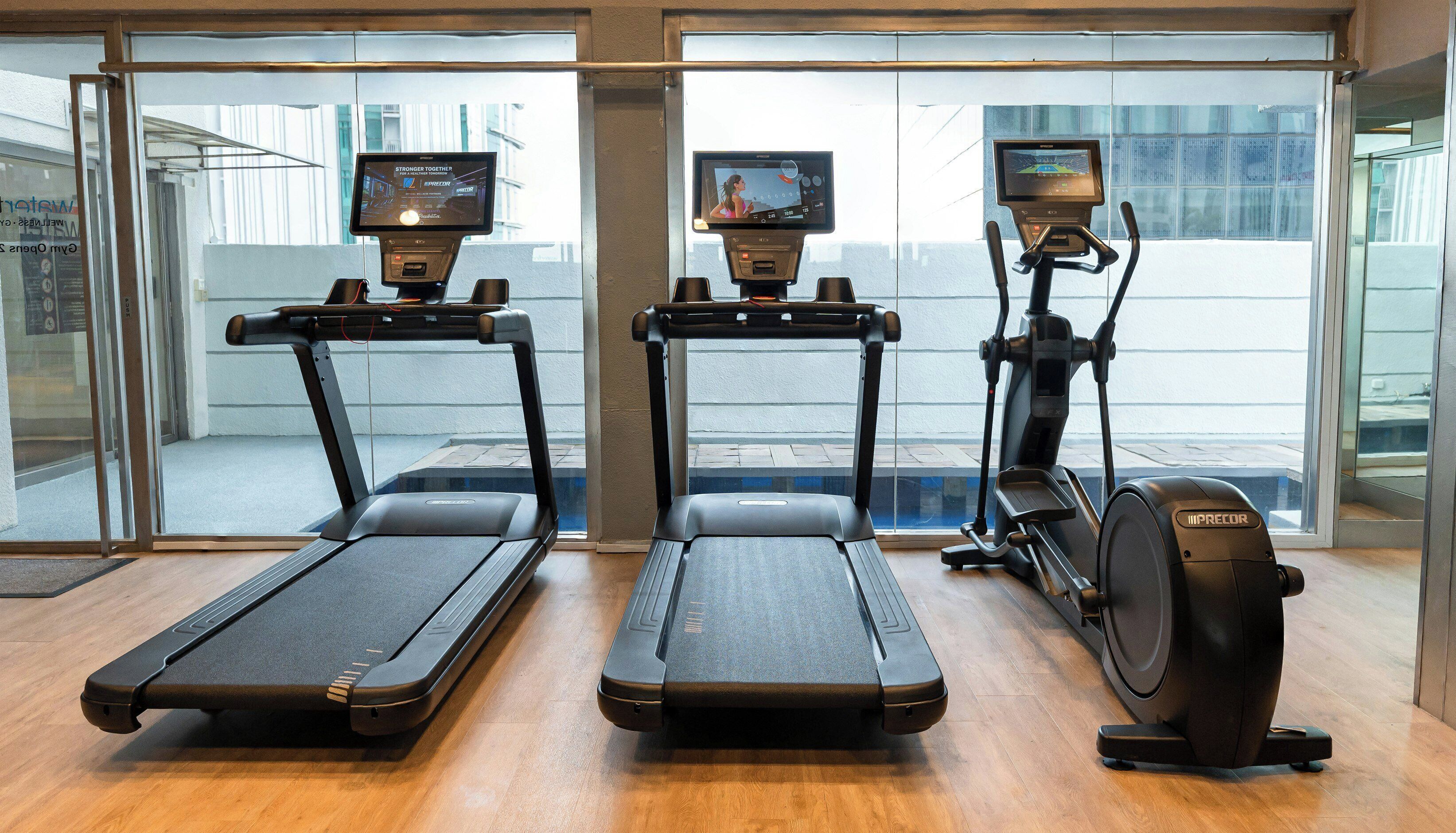 A gym with treadmills and an elliptical machine, large windows, and a view of the outside.